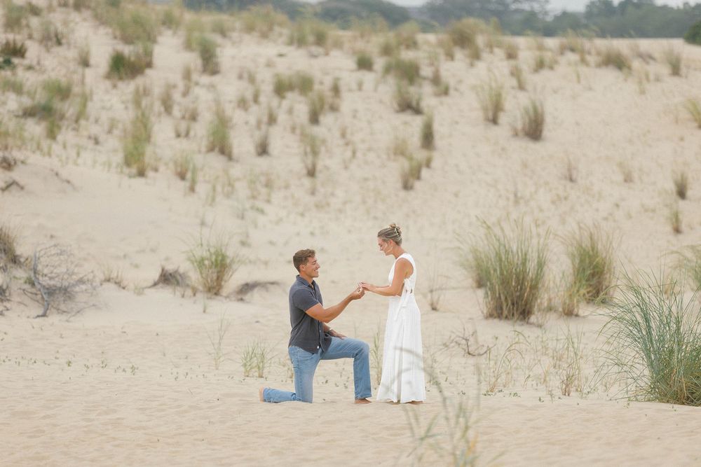 Couple sitting together on sandy dunes with beach grass in background.