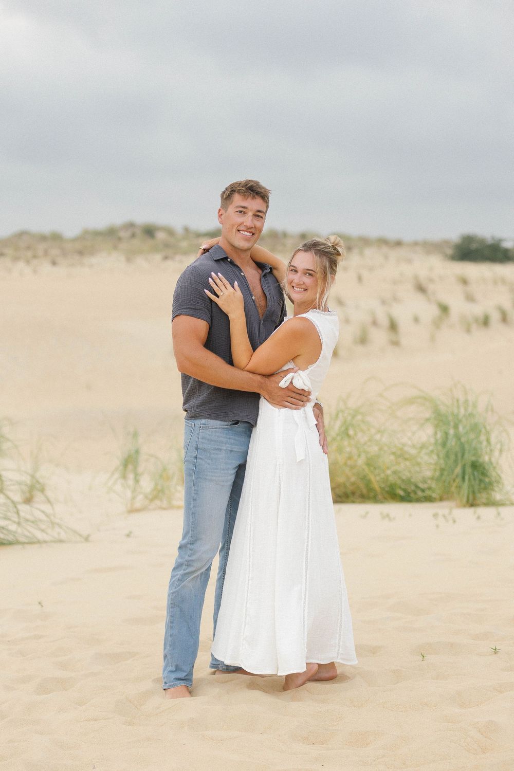 Couple embracing on sandy beach dunes in casual summer attire.
