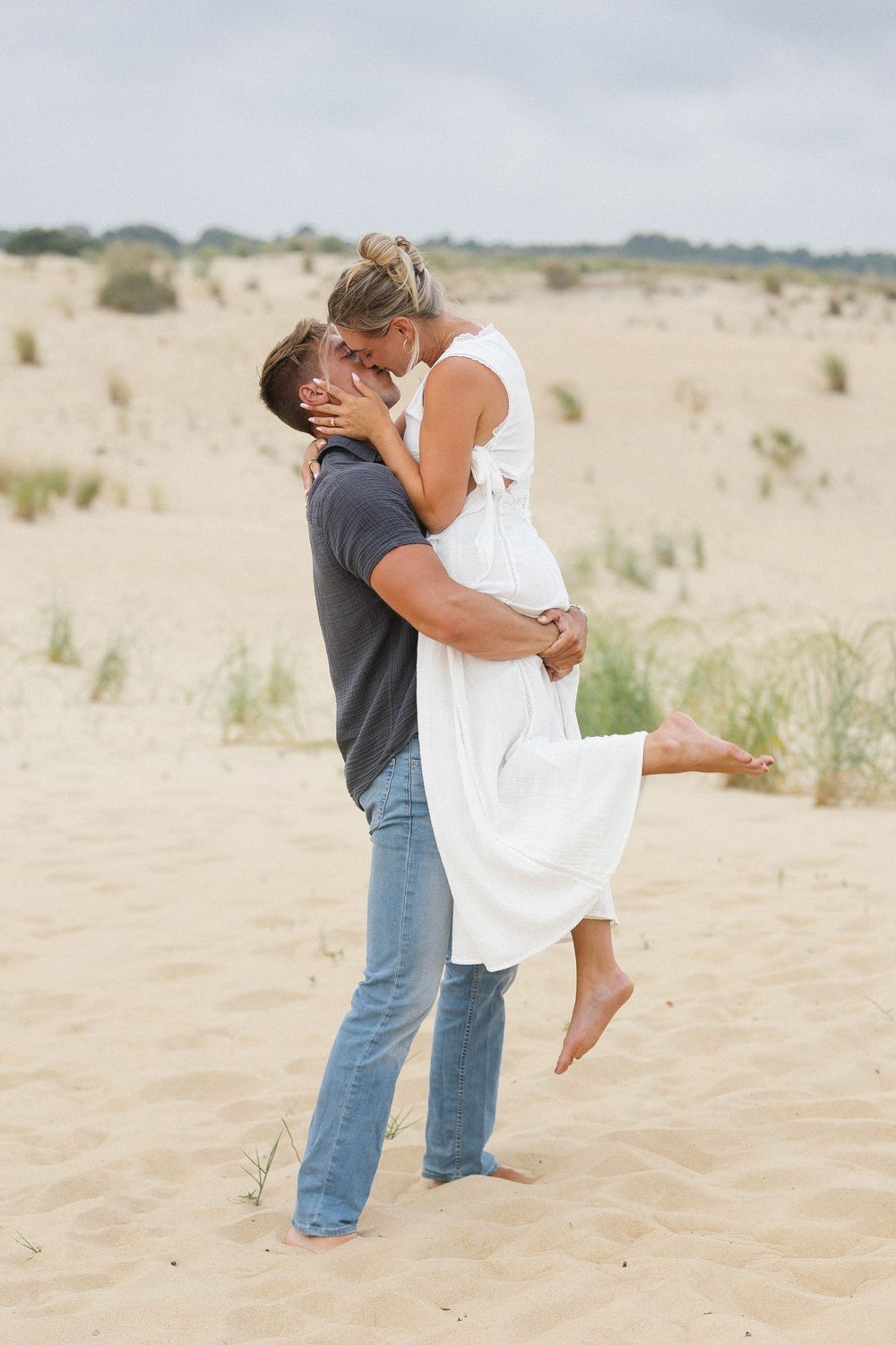 Playful couple dancing and embracing on sandy beach dunes.