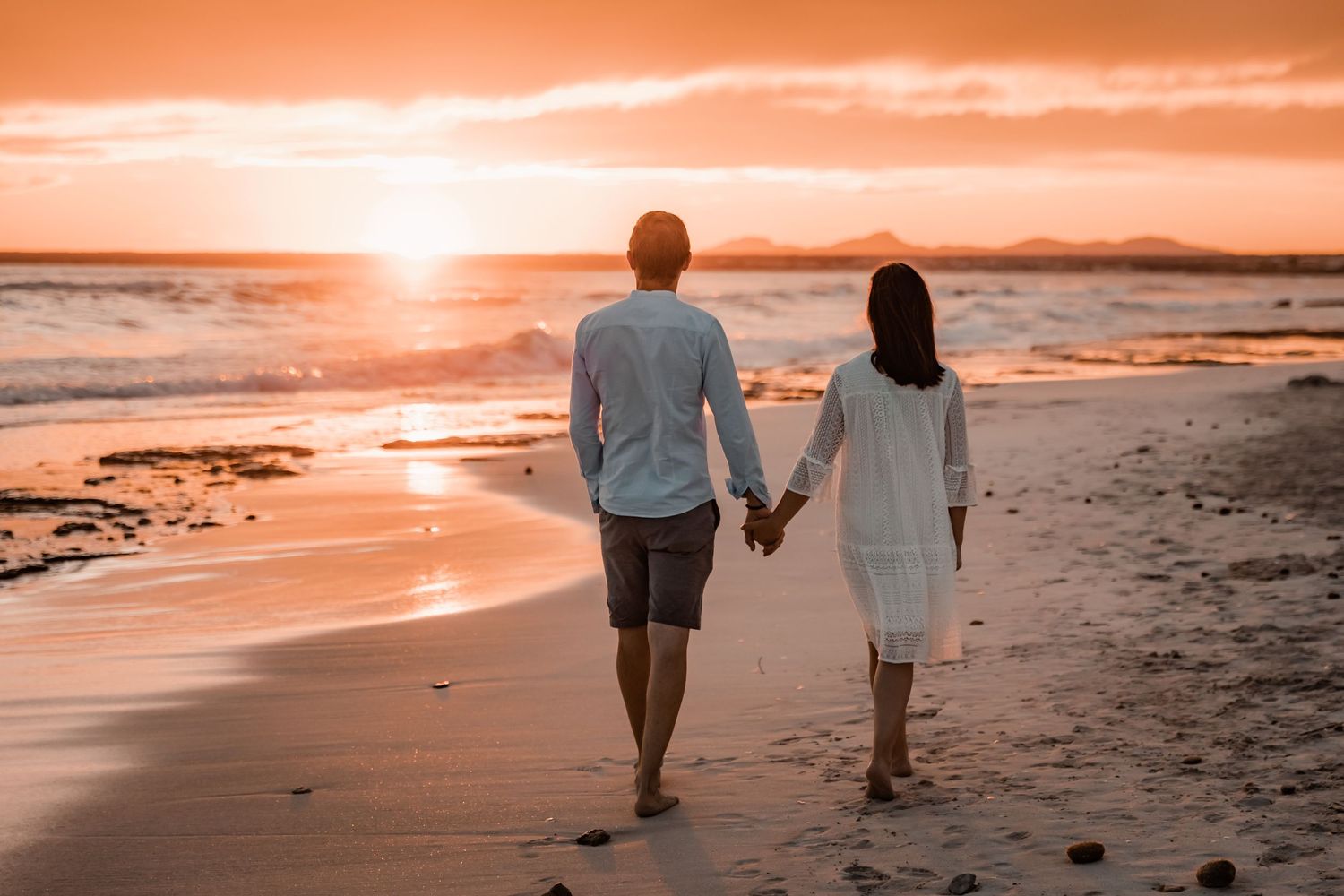 Candied lifestyle couple portrait of a man and a woman holding hands while walking on the beach at sunset in Mallorca.