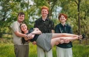 Four young redhead friends pose outdoors, two boys carrying a laughing girl while another stands behind them.