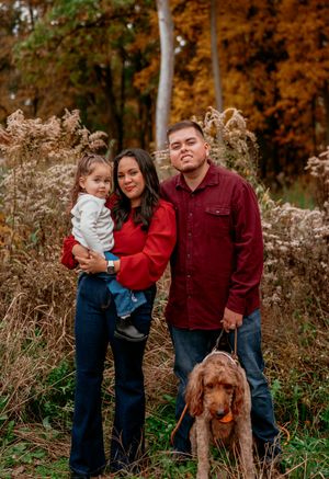 Family with a brown goldendoodle dog poses together outdoors during autumn with dried plants in background.