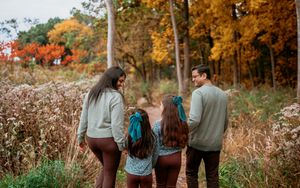 A couple walks hand in hand through a vibrant autumn forest with golden leaves and tall trees.