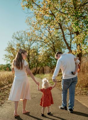 A family walking and playing together on a dirt path surrounded by autumn trees casting long shadows in golden light.