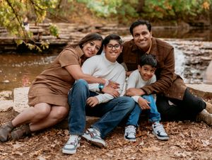 A family sits together on fallen autumn leaves near a stream for an outdoor portrait session.