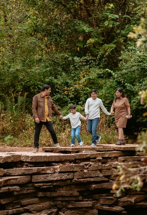 A family walks together along a rustic stone wall surrounded by autumn foliage in a park setting.