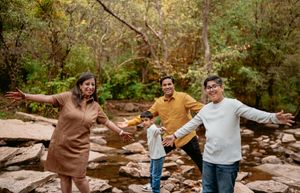A family enjoying time together on rocky terrain in a wooded natural setting, all with arms outstretched.