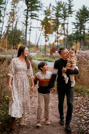 A candid family moment captured in a wooded area with pine trees and fallen leaves during autumn.