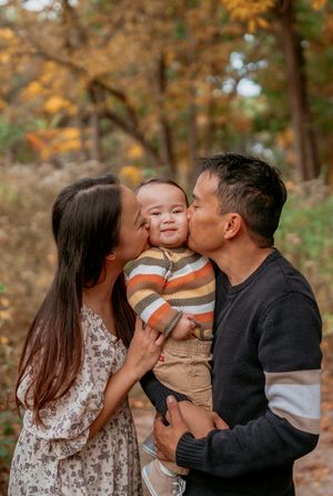 A family shares tender kisses and embraces during an autumn outdoor photoshoot with golden foliage in the background.