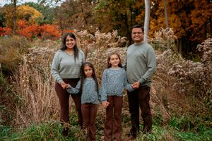 A family wearing coordinated blue and brown outfits poses together in a scenic autumn setting with fall foliage.