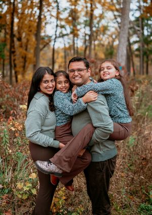 A group shares warm embraces and laughter together during an autumn photoshoot in a wooded setting with golden foliage.
