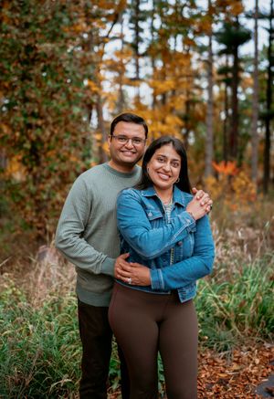 A couple embraces while standing in a forest with autumn foliage and fallen leaves creating a romantic outdoor setting.