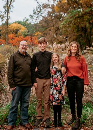 A group of four people standing together outdoors during autumn with colorful fall foliage in the background.