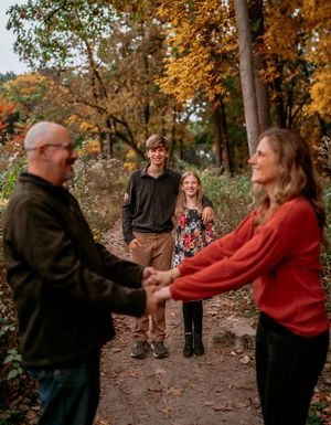 A couple dances together on a wooded path surrounded by autumn trees with golden leaves.