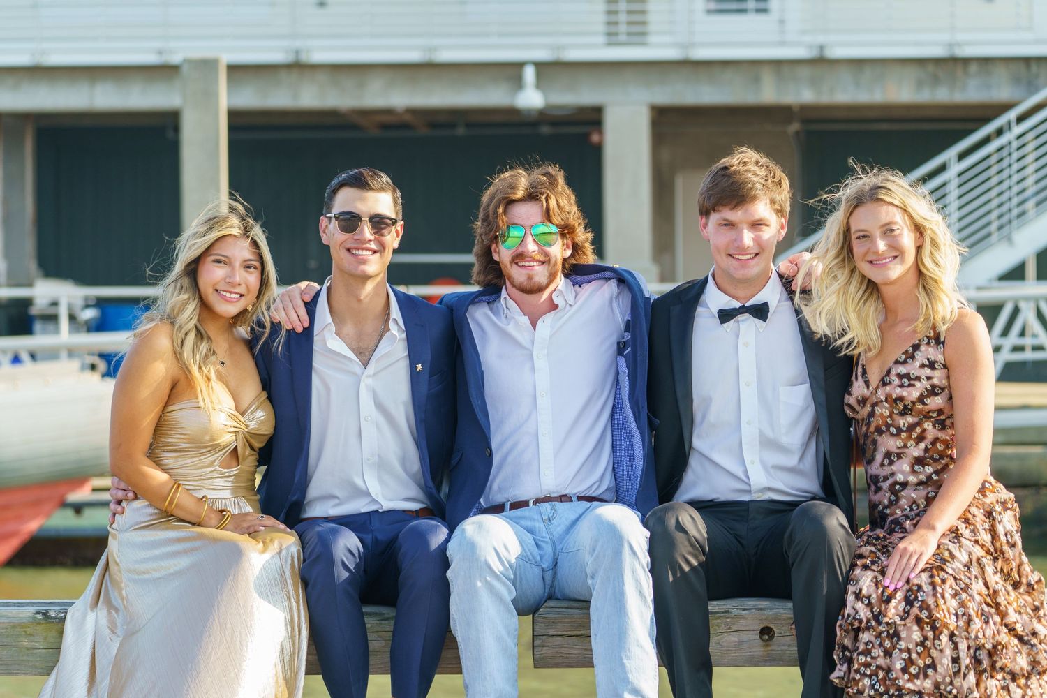 Group of friends posing together outdoors on a sunny day wearing formal and casual attire.