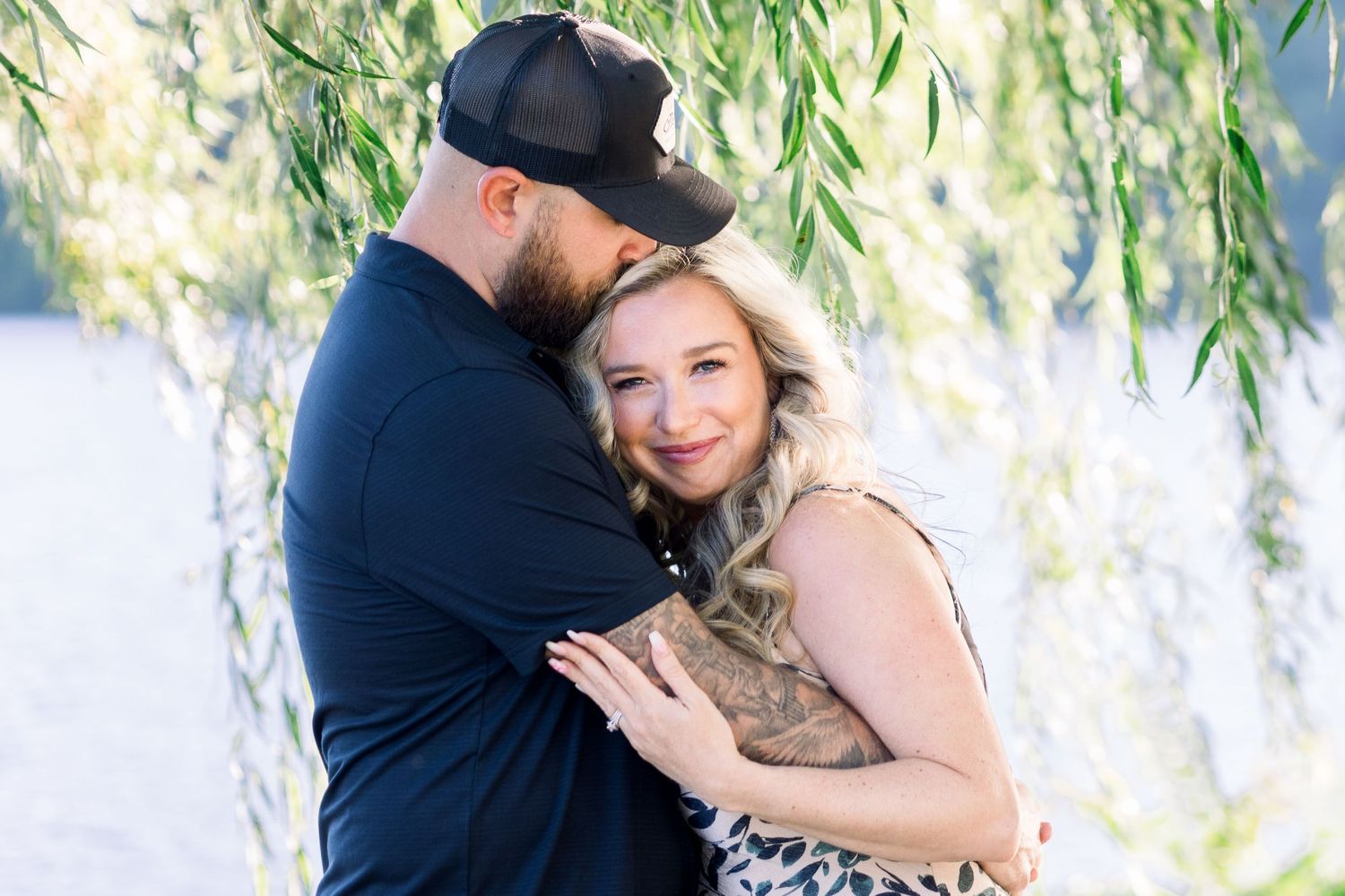 Couple sharing tender moments under willow trees near water.