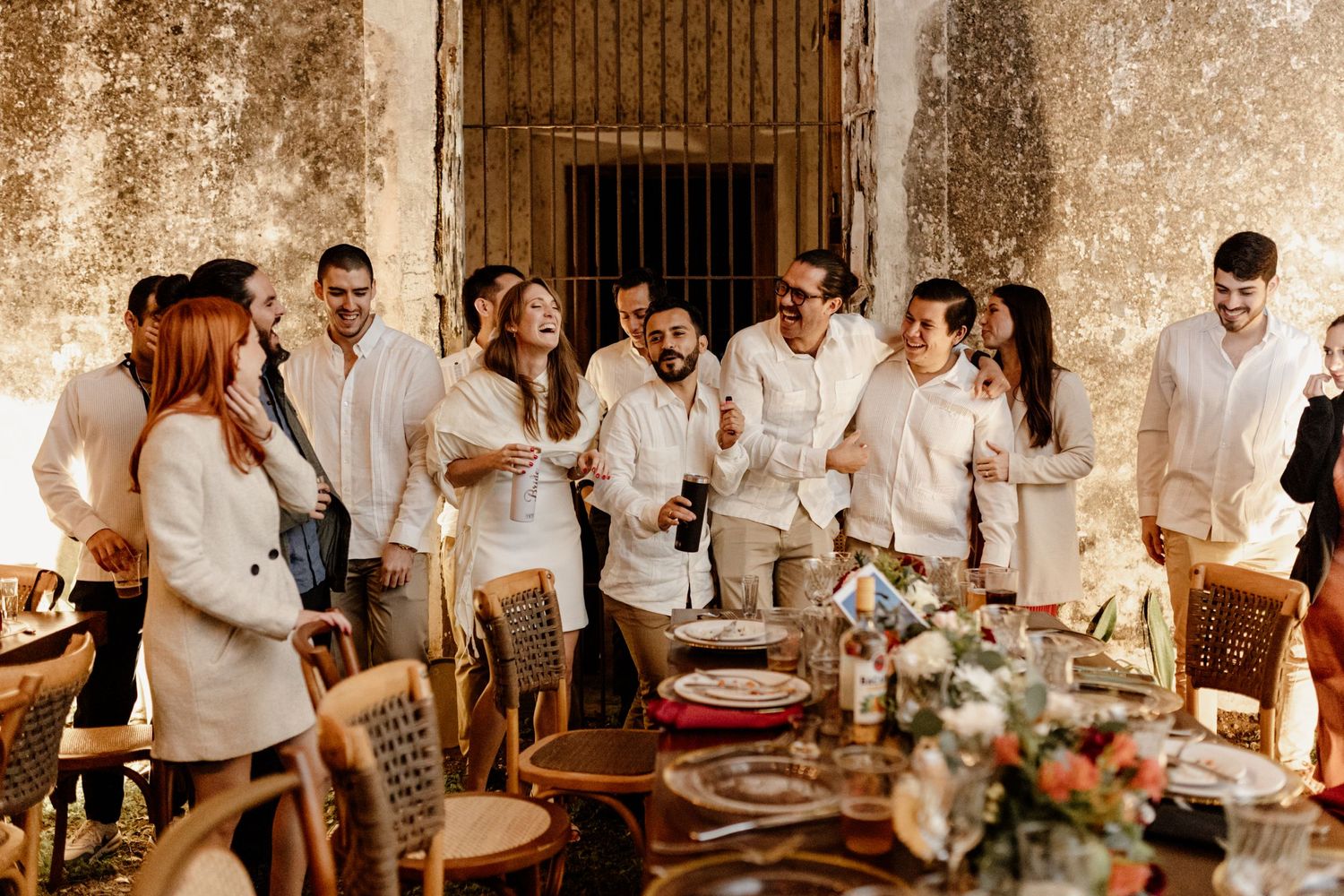 A group of guests in white attire gathered around an elegant table setting at an outdoor celebration.