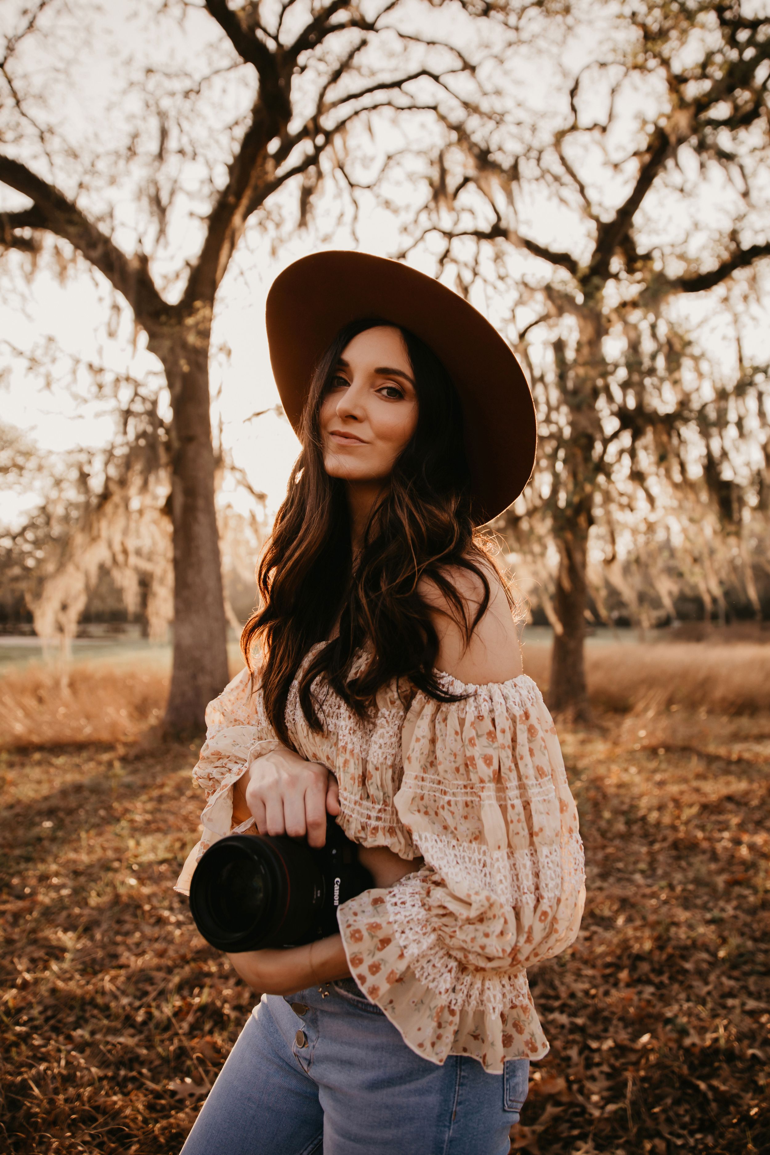 Portrait of woman in hat and off-shoulder top against autumn trees.