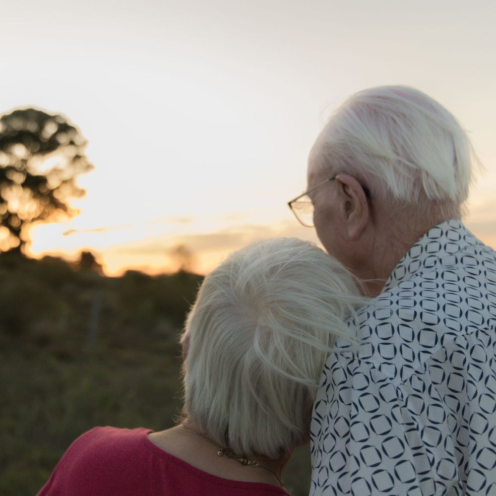 Elderly couple sharing tender moment against sunset backdrop.