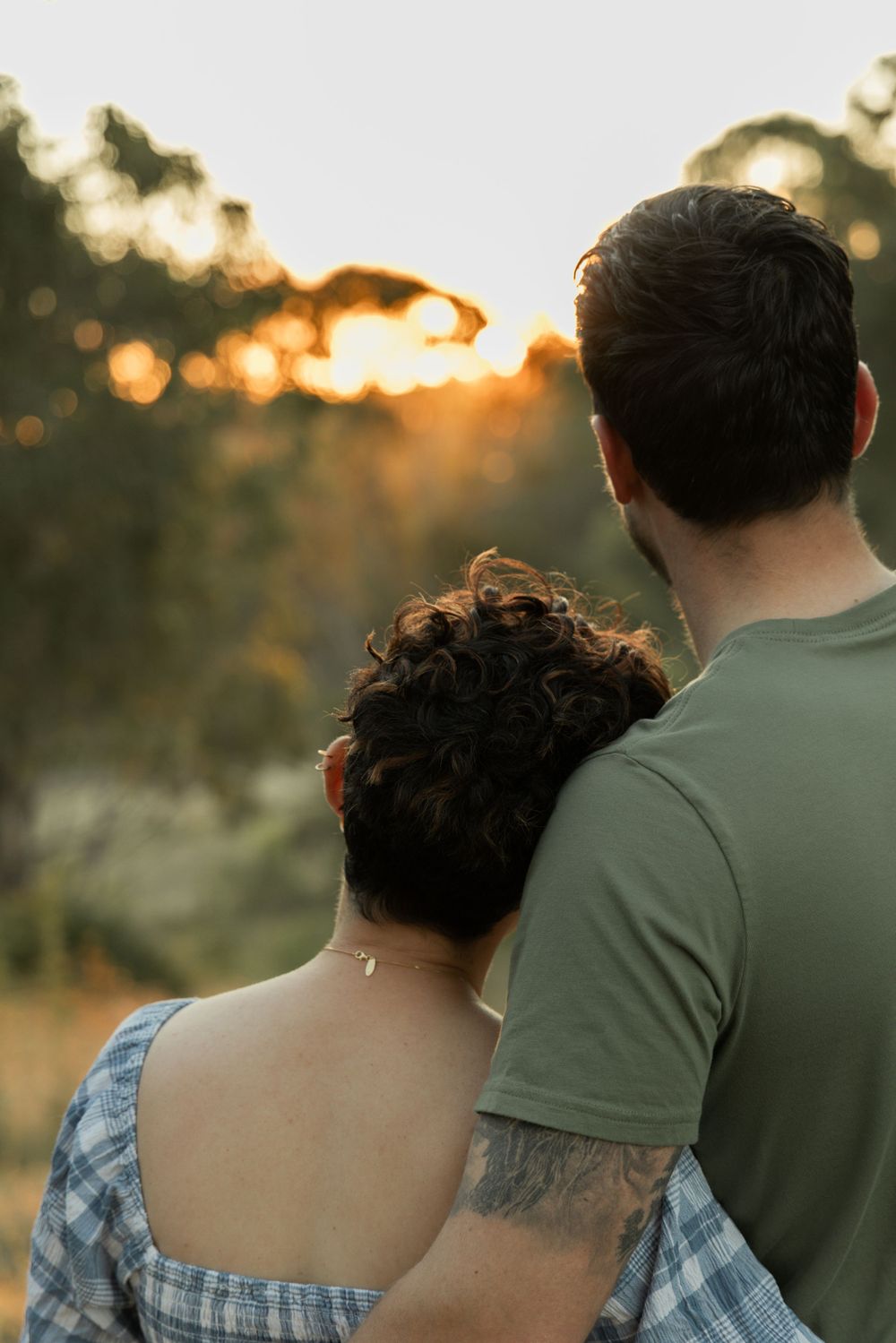 Couple watching sunset together with visible tattoo on arm in casual attire.