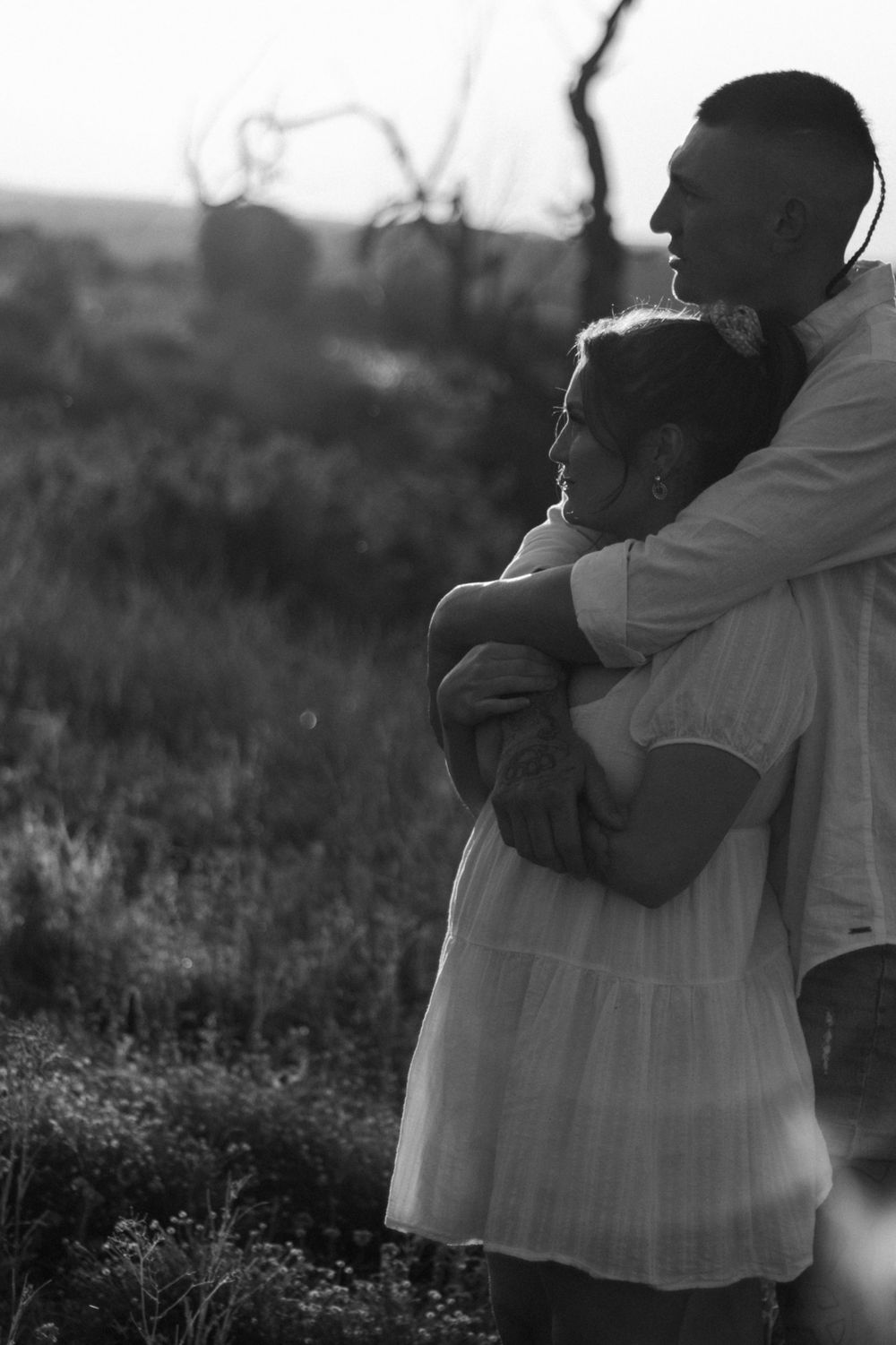 Black and white silhouette of couple embracing in nature during sunset.