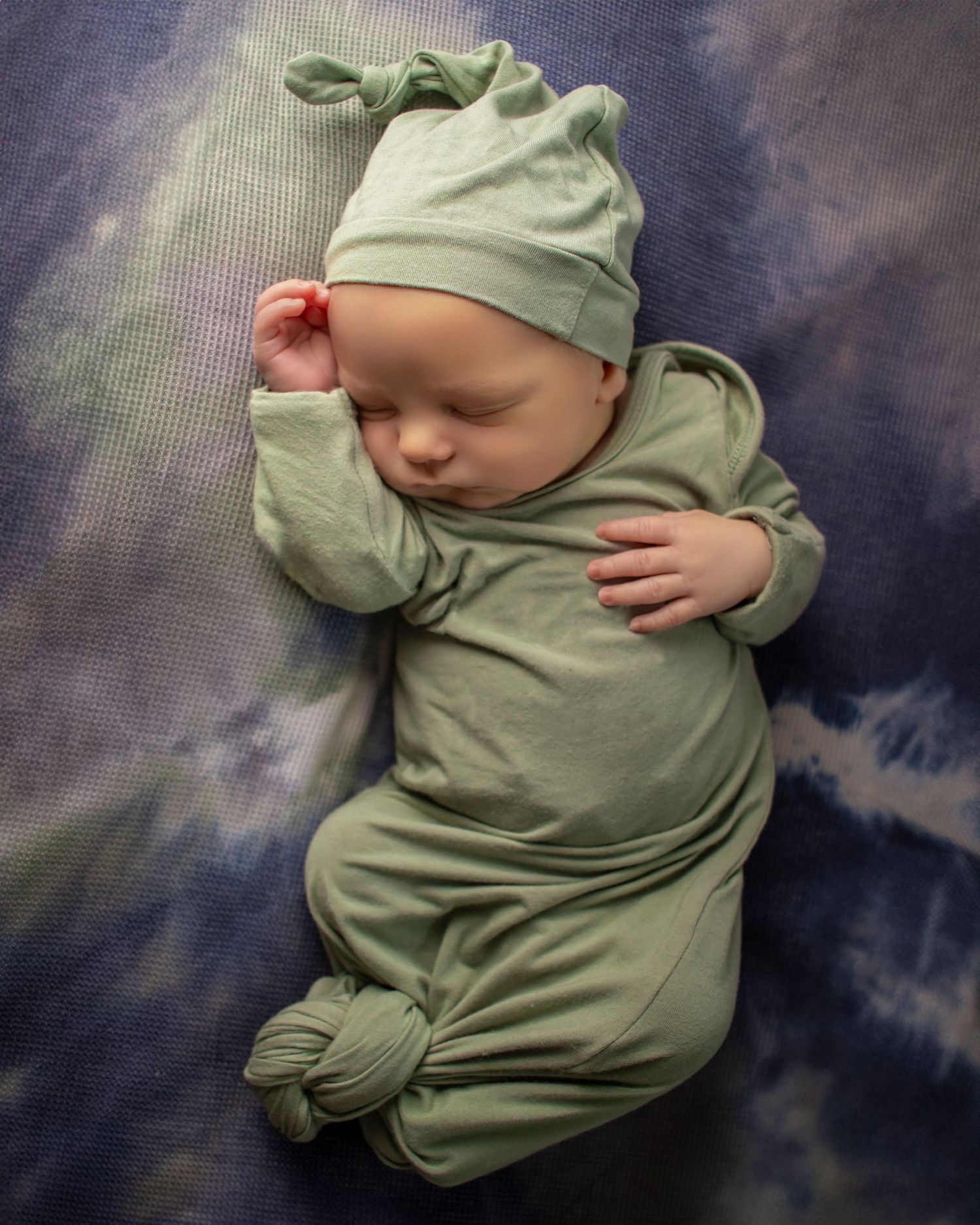 A newborn boy lays sleeping on a tie dye background