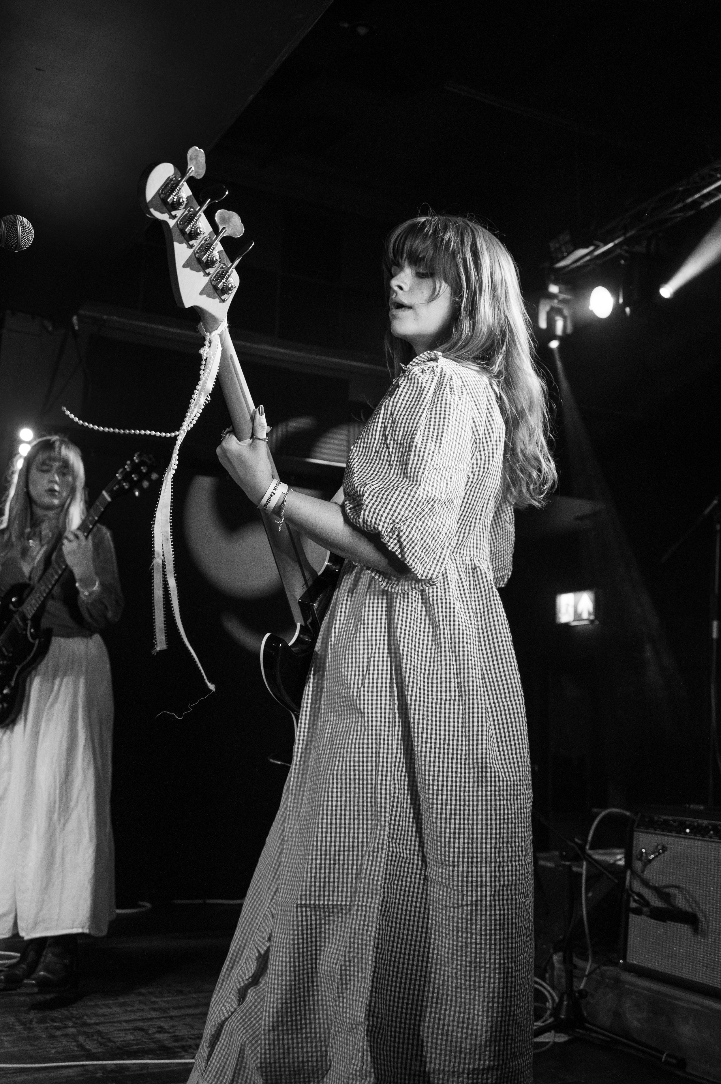 Musician in gingham dress performs with guitar on dimly lit stage.