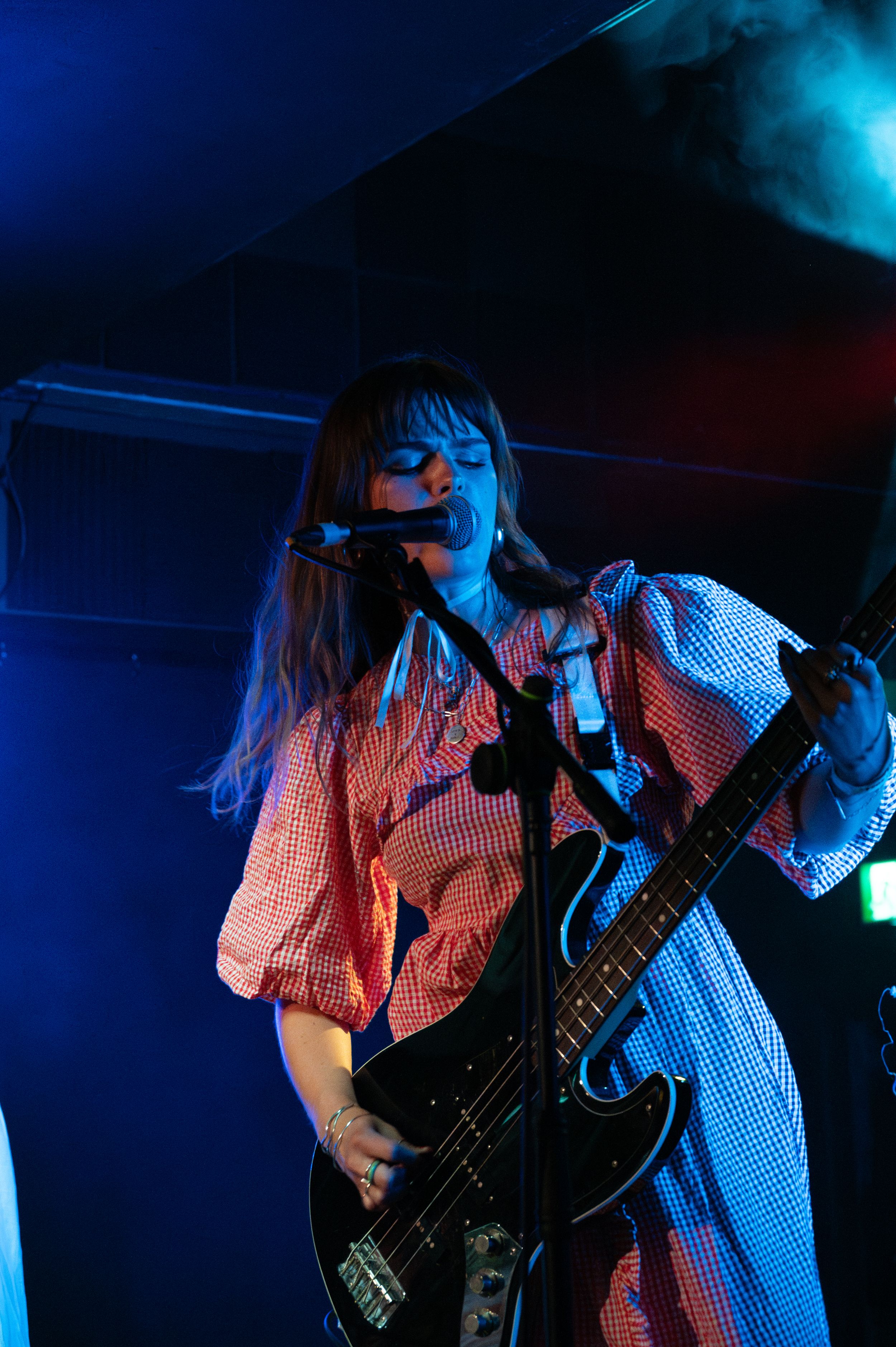 Bassist performs in checkered dress under blue stage lighting.