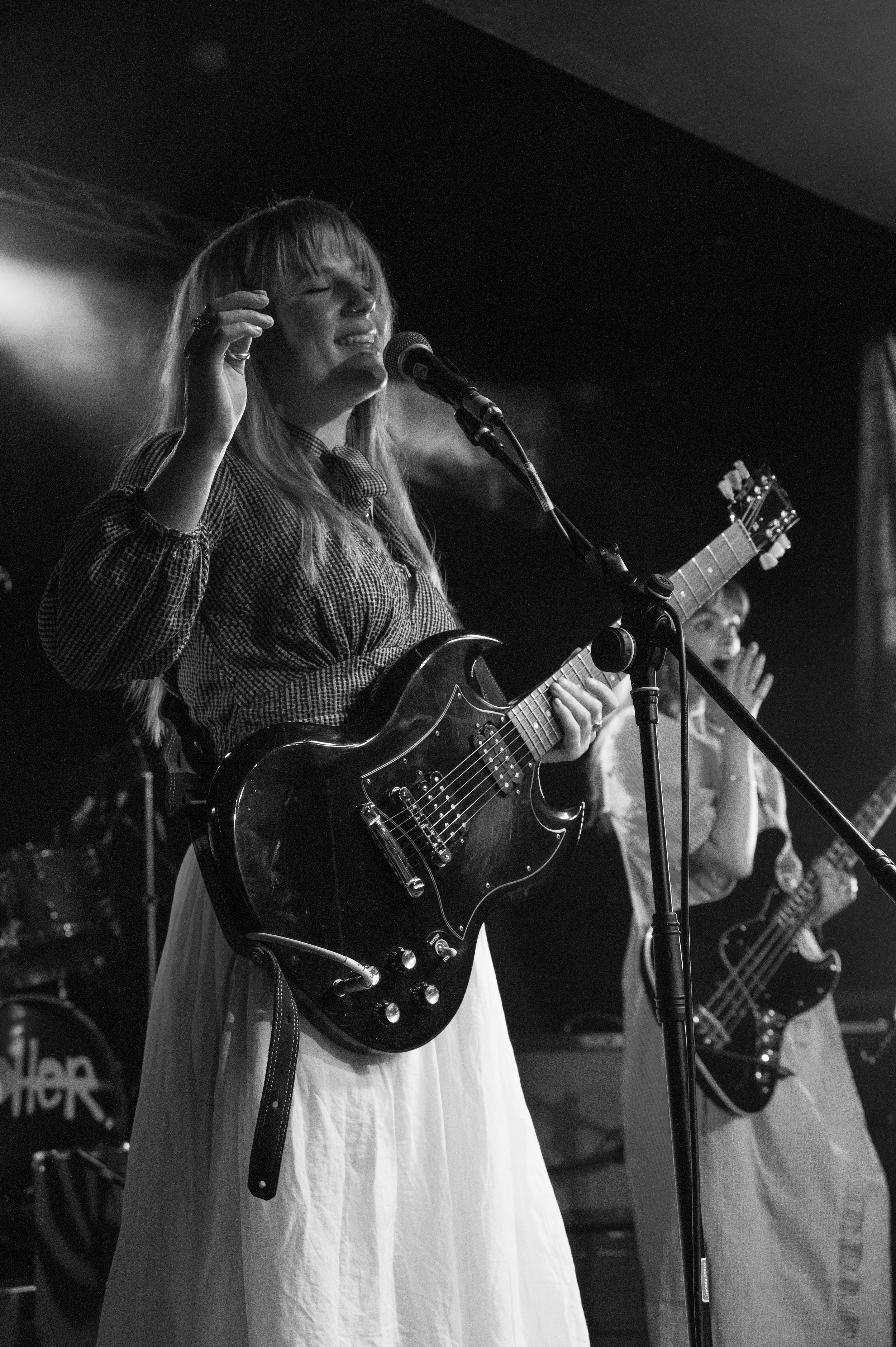 Guitarist in vintage-style dress performs with electric guitar under stage lights.