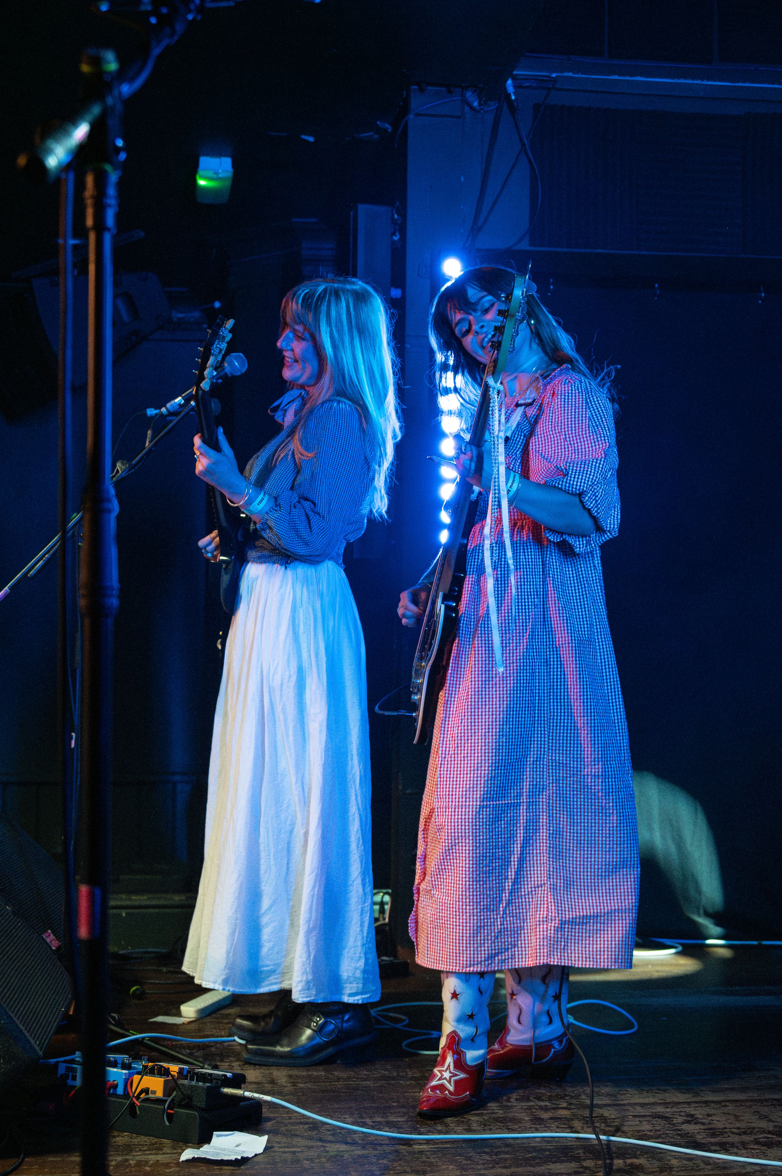 Two performers in long dresses singing into microphones on stage with blue lighting.