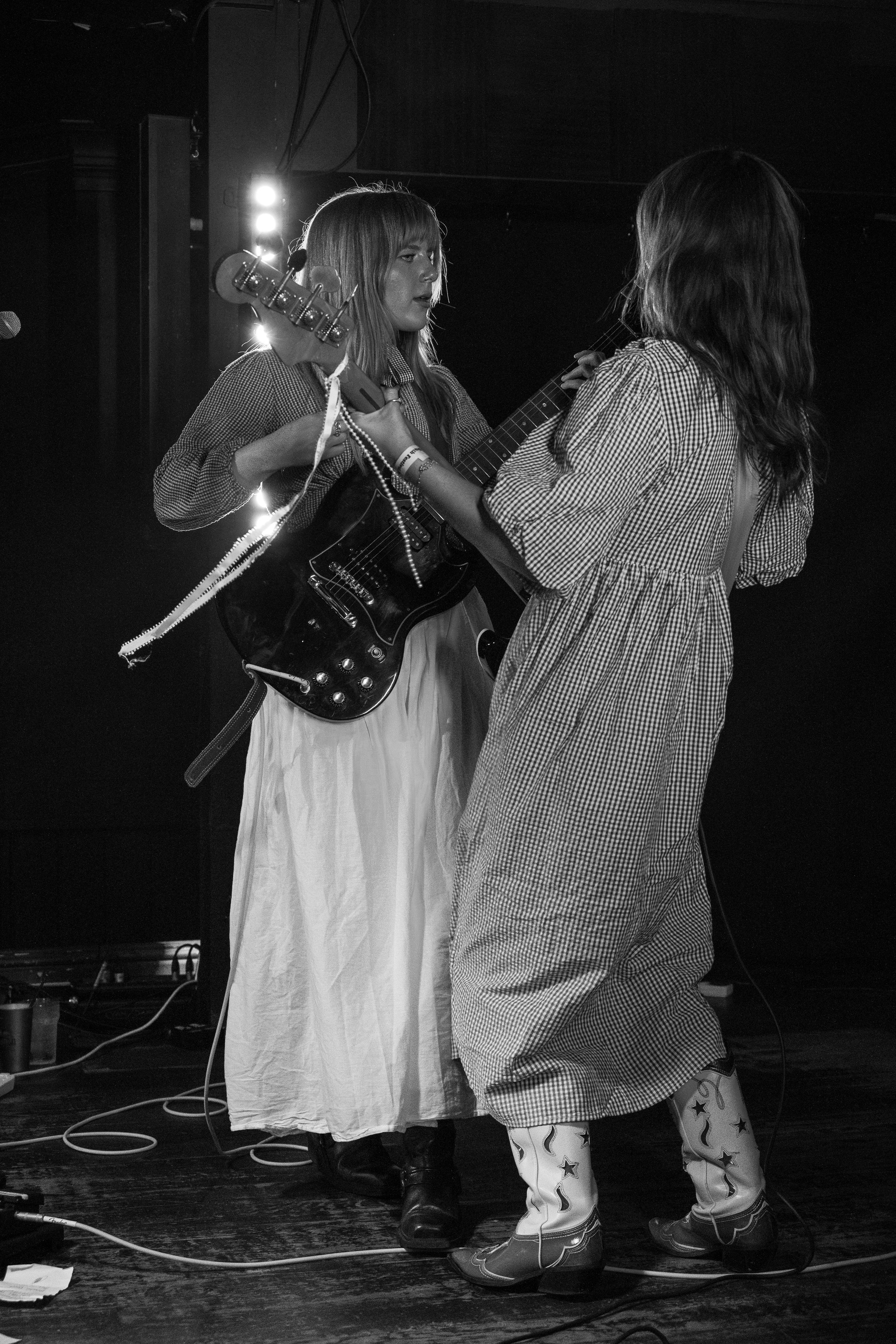 Black and white image of two performers in dresses with guitar on dimly lit stage.