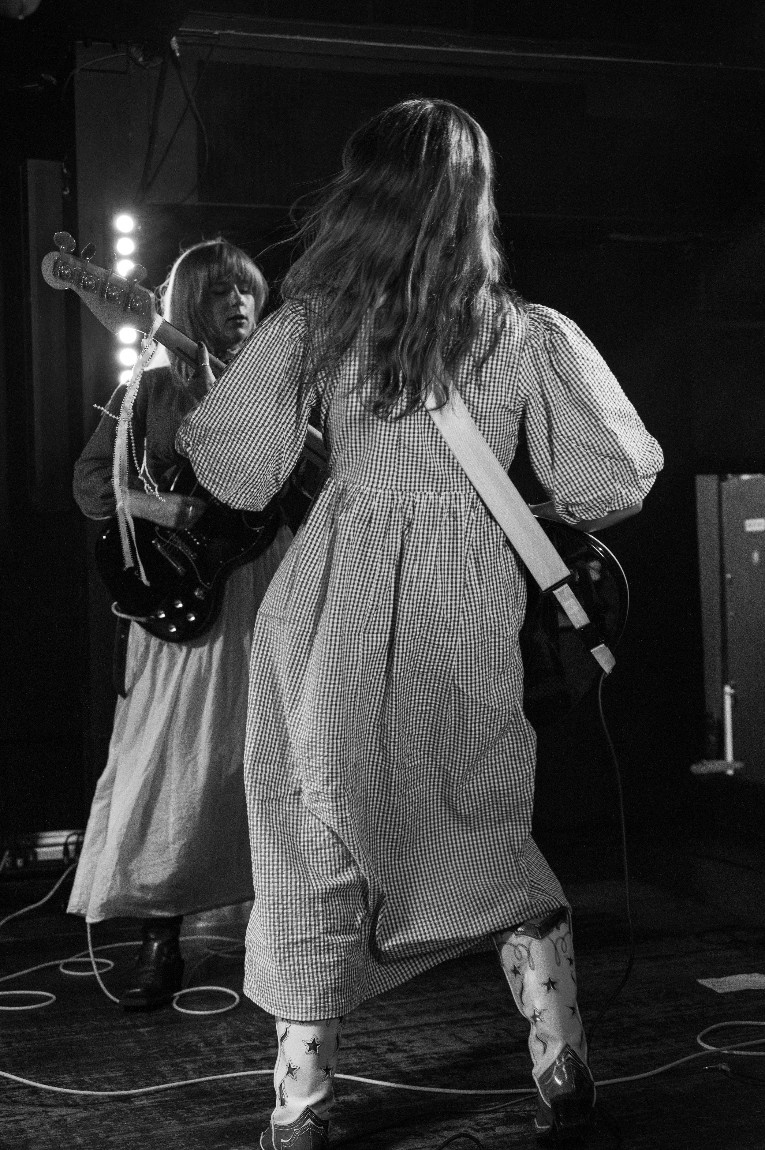 Black and white concert photo showing performers in patterned dresses from behind on stage.