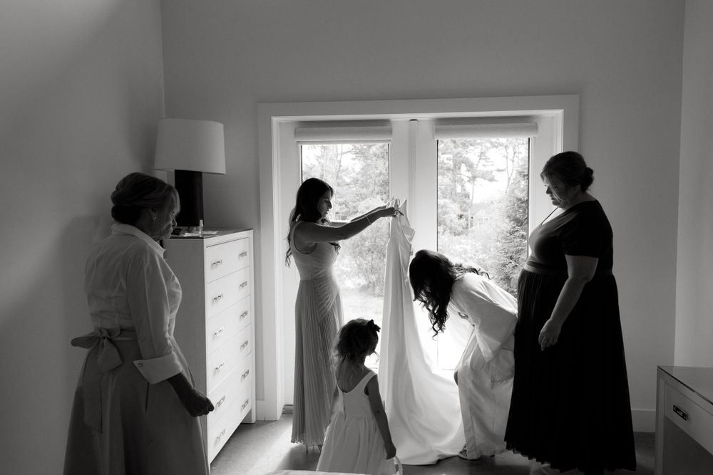 Wedding preparation scene with people helping with the bridal dress near a window.