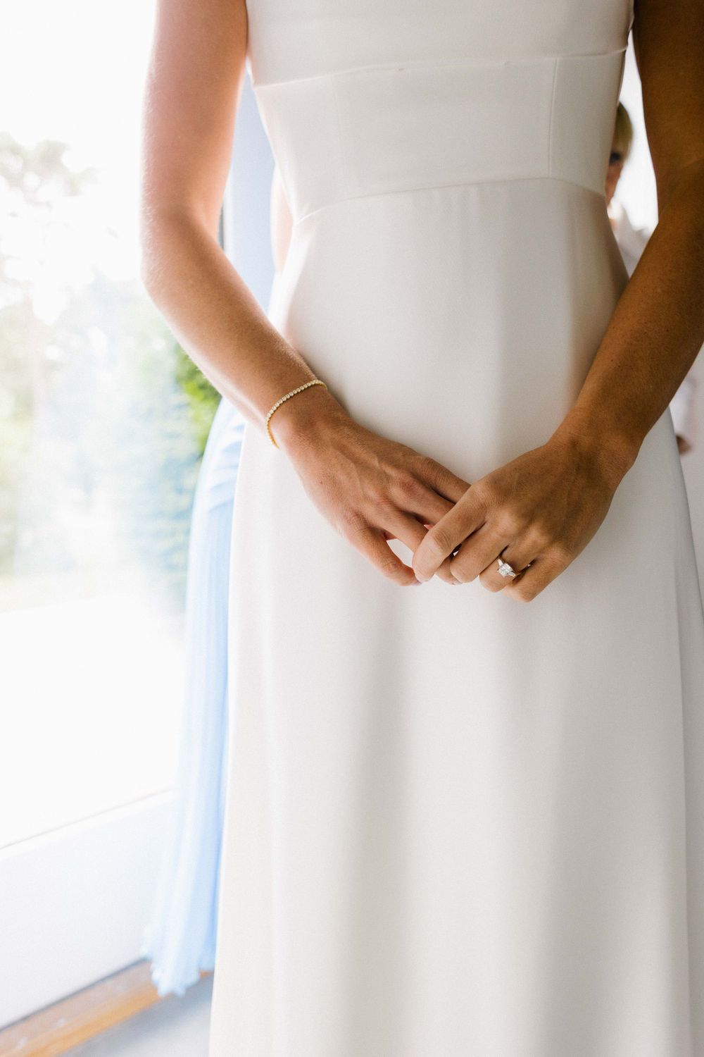 Close-up detail of hands clasped together against a white wedding dress.