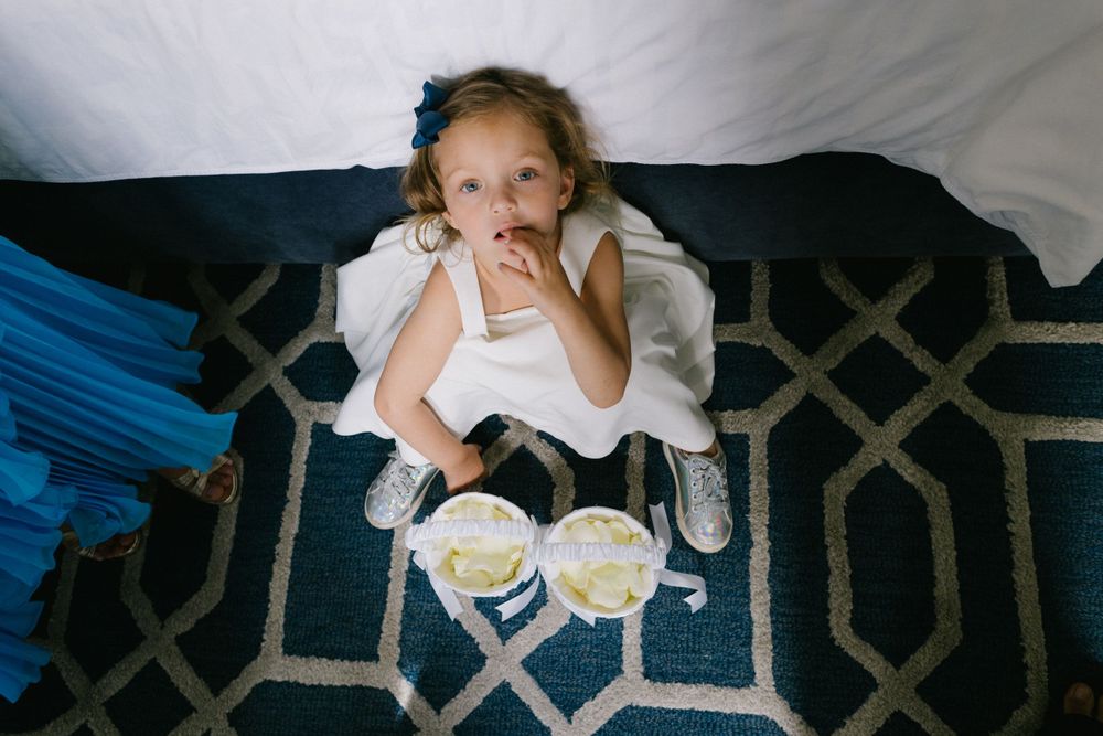 A white-dressed figure sits on a patterned blue rug with two plates in front.