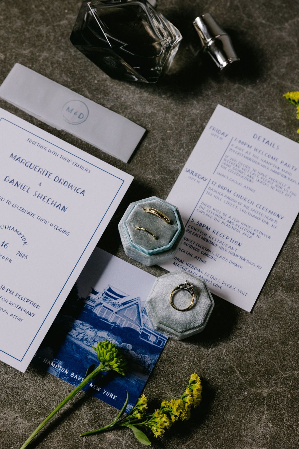 Elegant wedding invitations and ring boxes arranged with yellow flowers on dark surface.