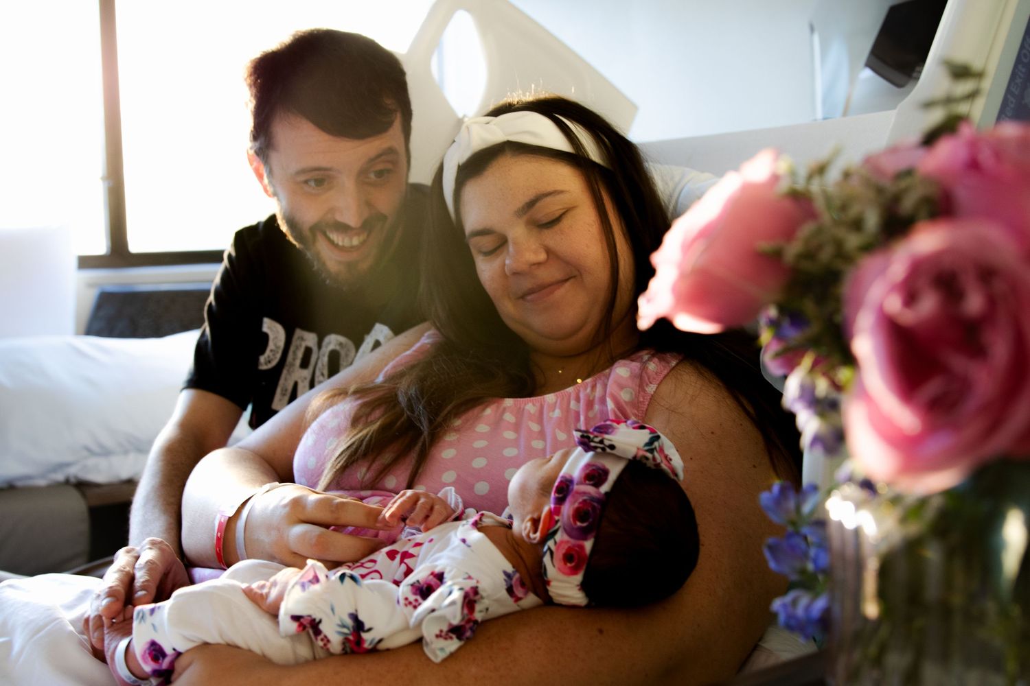 Mom and dad with newborn baby in the hospital and pink flowers in the forefront