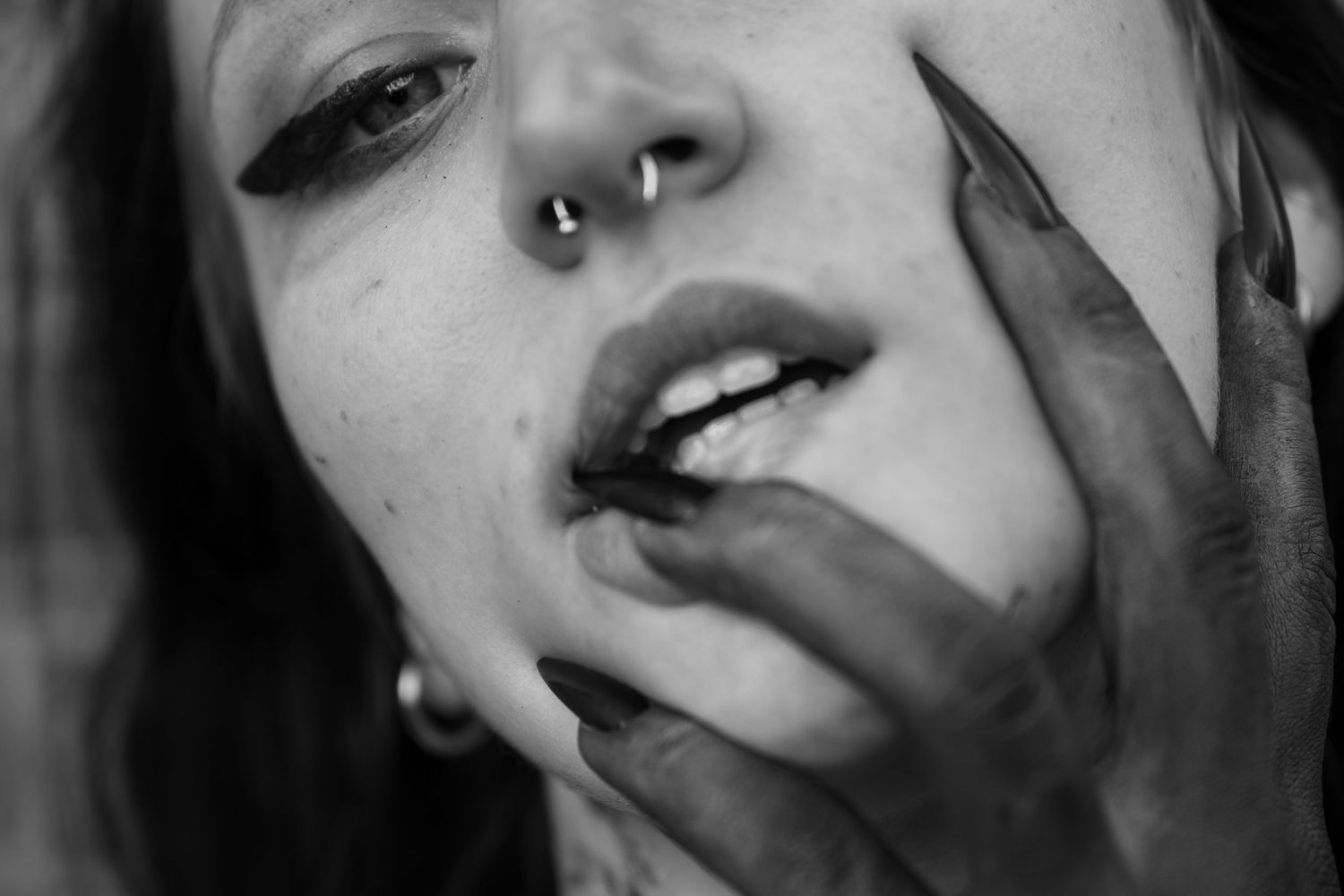 Black and white close up portrait showing nose piercing and dark fingernails touching lips.