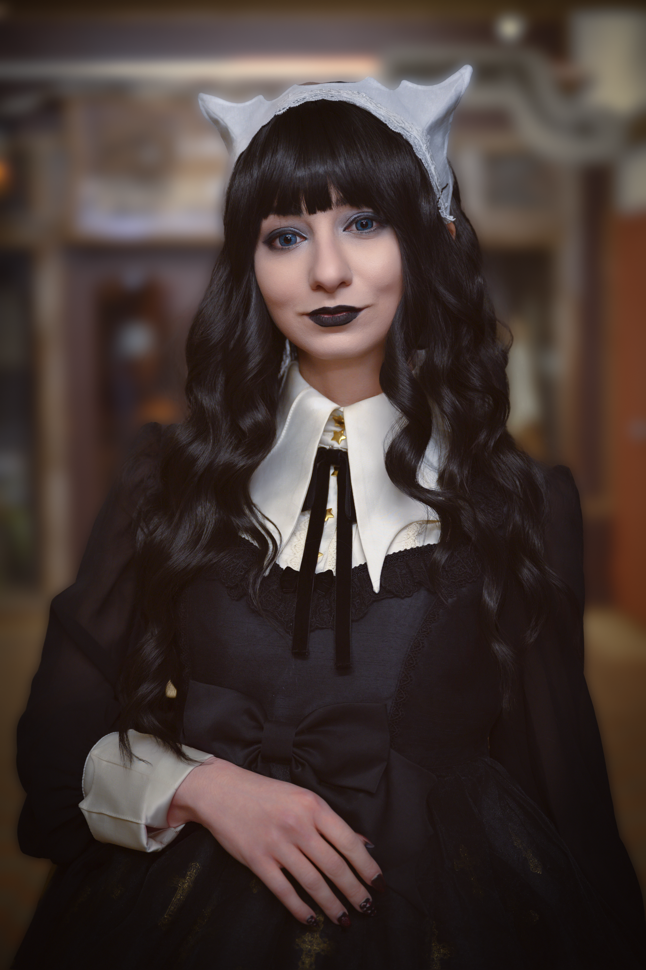 Gothic cosplay outfit featuring black dress with white collar, black bow tie, cat ears headband and dark makeup.