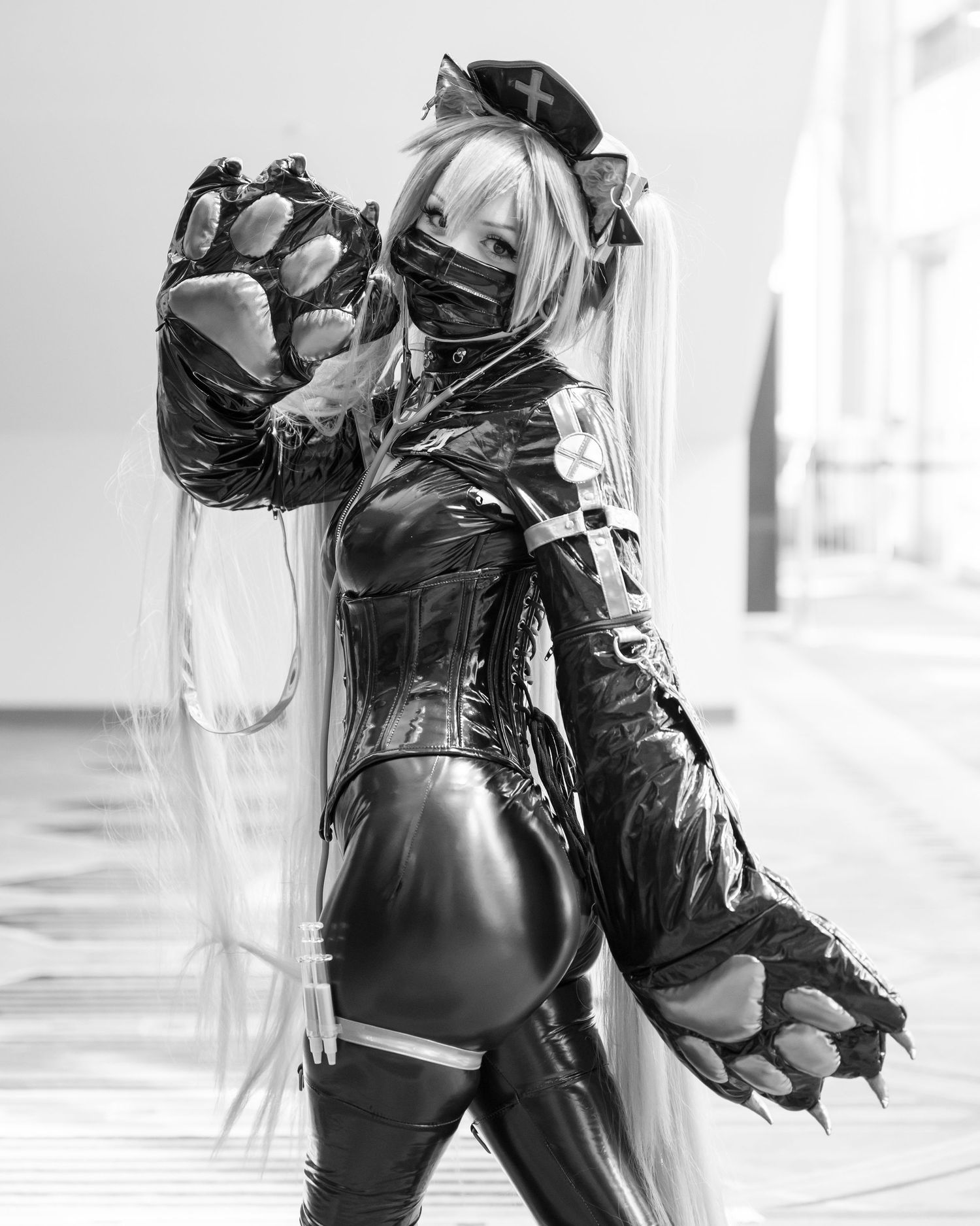 A cosplayer in a black latex bodysuit and mask strikes a dramatic pose against a white background.