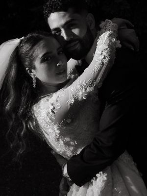Black and white wedding portrait of bride in lace gown and groom in suit embracing romantically outdoors.