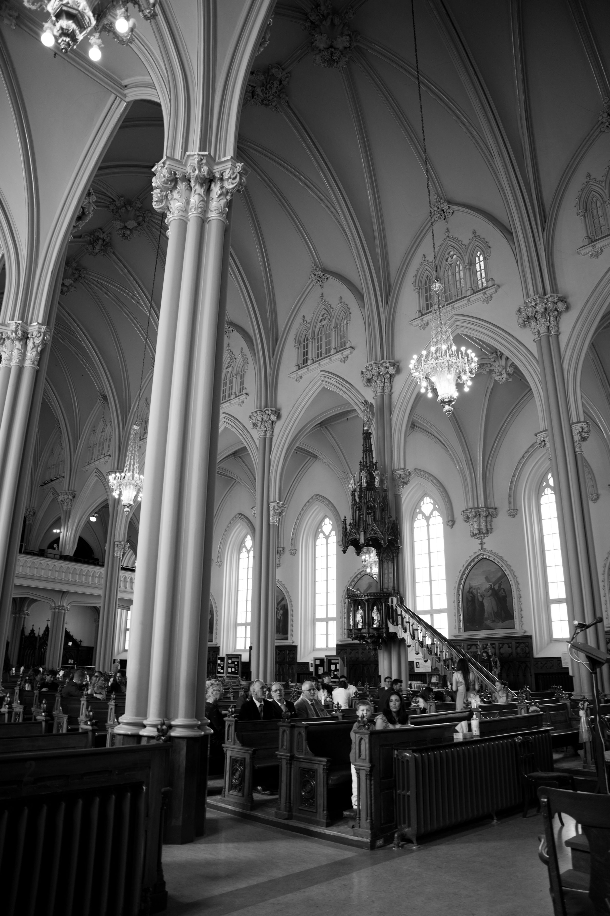Interior view of a Gothic church with vaulted ceilings, ornate columns and crystal chandeliers in black and white.