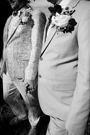 A black and white detail shot of two people in complementary wedding suits with floral boutonnieres.
