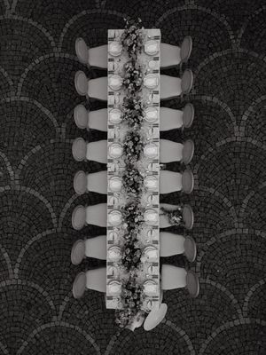 Overhead view of an elegant table setting with white chairs and floral centerpieces on a dark mosaic floor pattern.