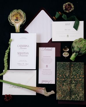 Elegant wedding invitation suite featuring white cards with pink text and floral accents laid out on a dark surface.
