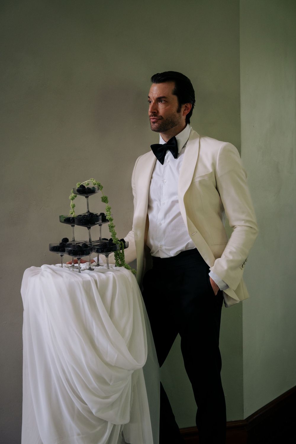 A formal wedding setup with white tablecloth and black accents against a minimalist green backdrop.