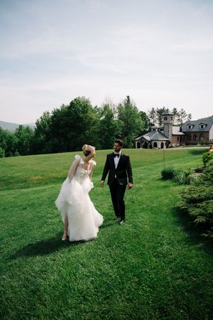 A couple walks together across a scenic hilltop lawn with a grand estate house visible in the background.