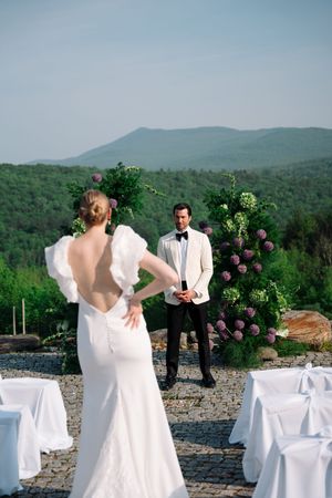 Wedding couple shares a romantic first look moment against a backdrop of mountains and decorated white chairs.