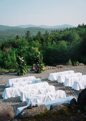 Outdoor wedding ceremony setup with white-covered chairs arranged on a stone patio overlooking mountain views.