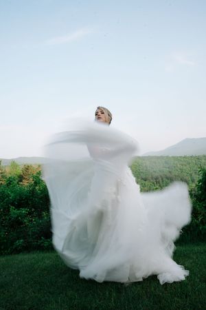 A bride in a flowing white wedding dress twirls gracefully across a green hillside in a series of motion-blurred photos.